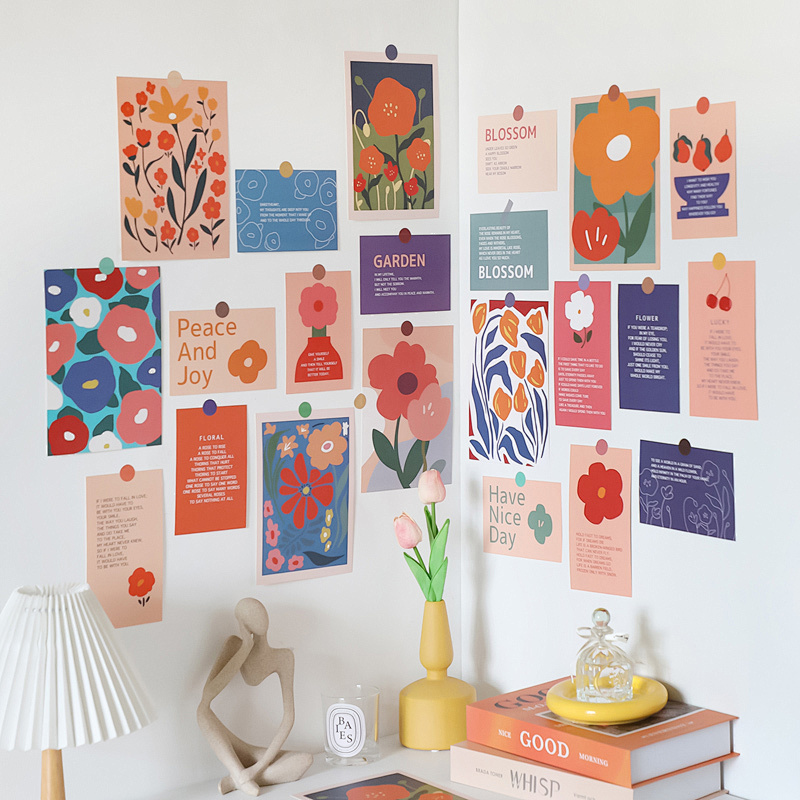 A wall decorated with colorful floral-themed posters, inspirational quotes, and art prints, accompanied by a shelf holding books, a vase with tulips, a lamp, and decorative items.
