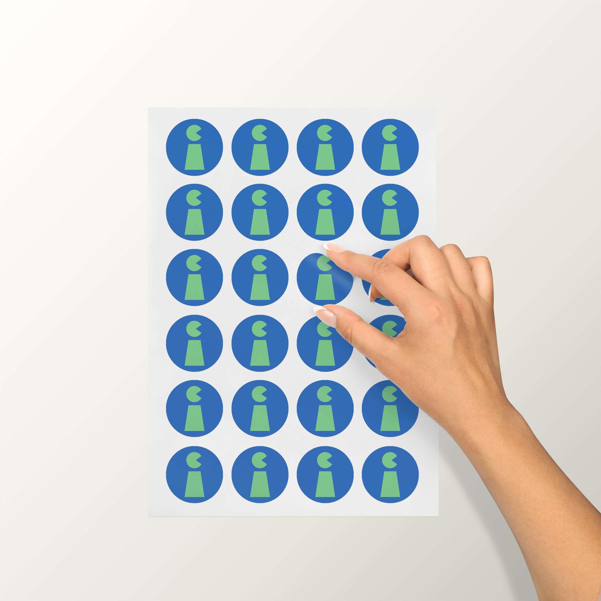 A hand peeling a blue and green circular sticker from a sticker sheet.