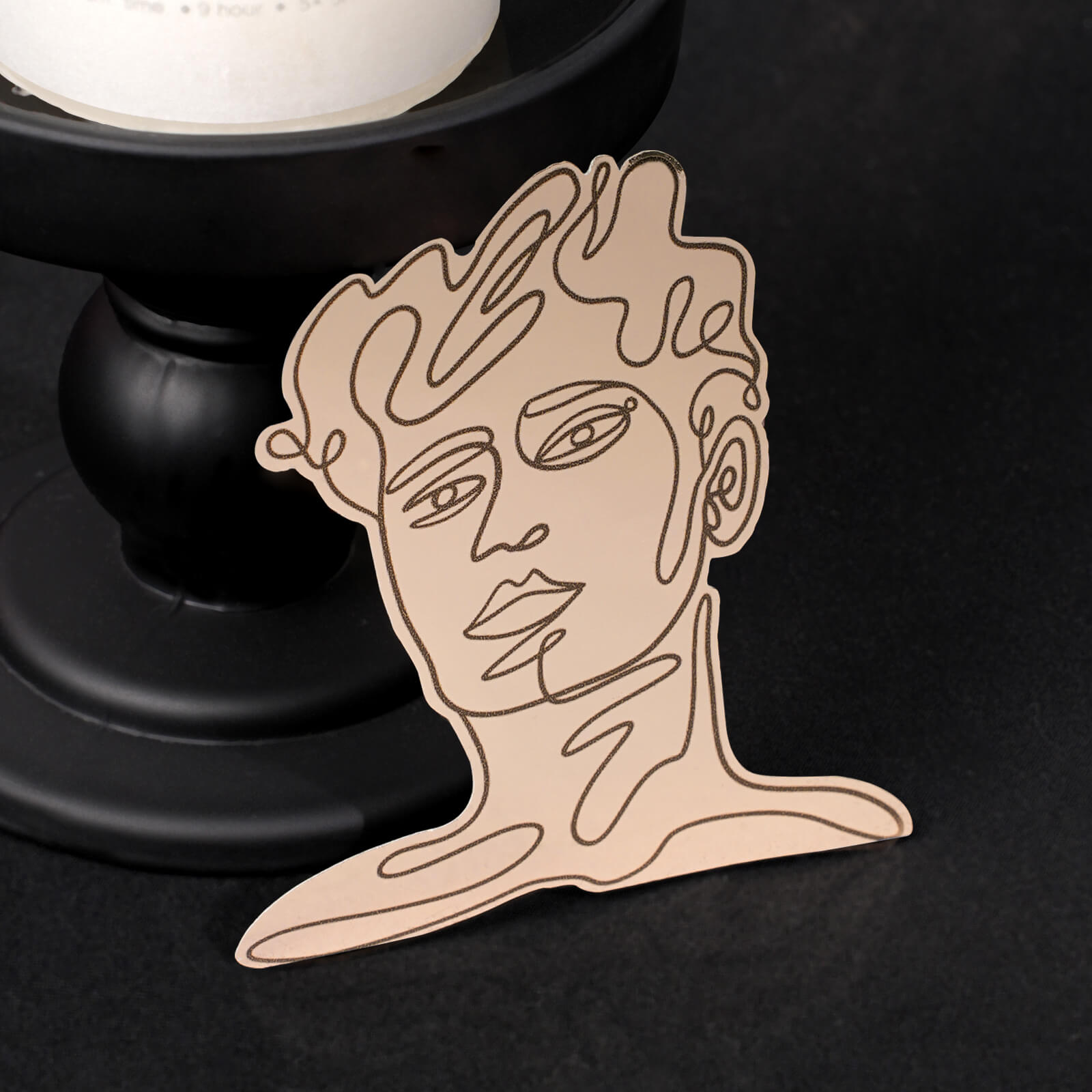 Vinyl sticker with a minimalist line drawing of a human face, placed near a black candleholder.