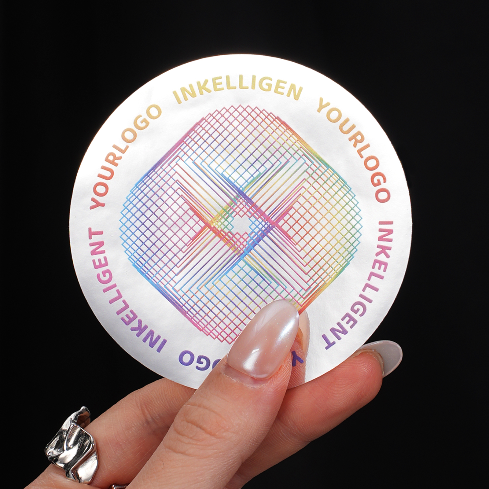 Round vinyl sticker with a metallic silver finish, colorful geometric design, and text, held between fingers.