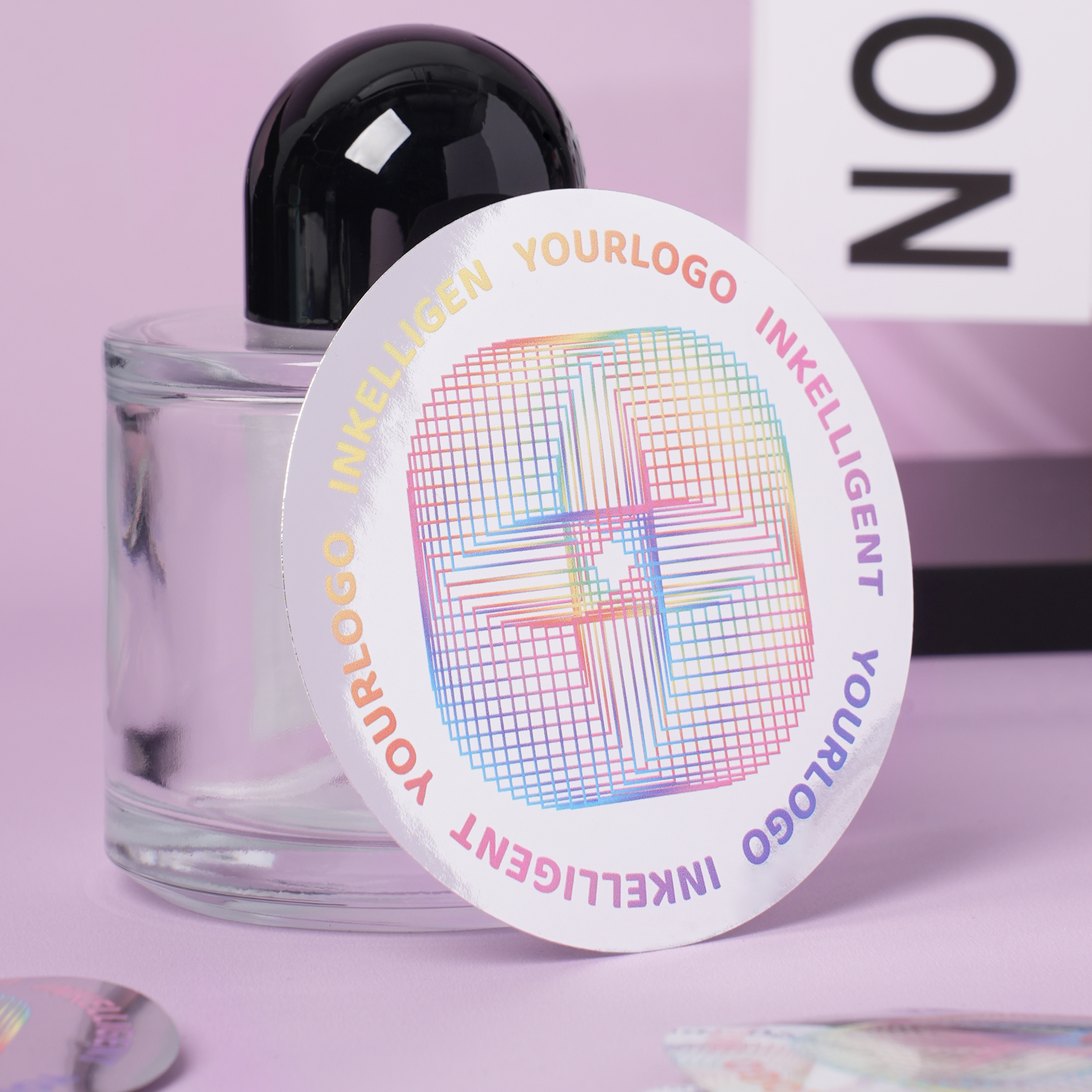 Round metallic silver vinyl sticker with a colorful geometric design and text, leaning on a glass bottle.