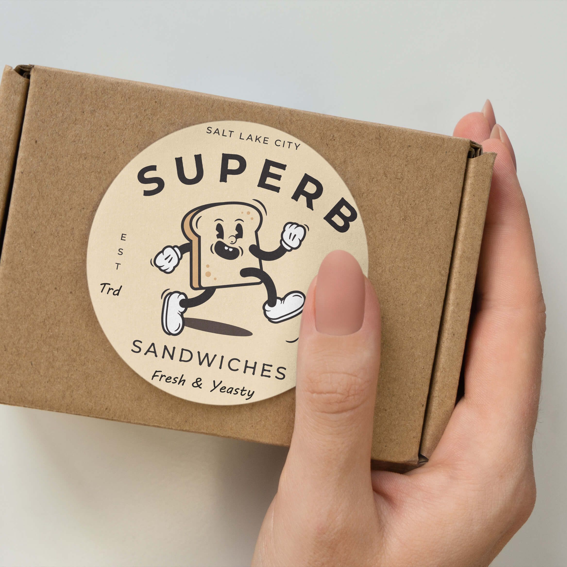 Hand holding a brown box with a sandwich-themed sticker design.