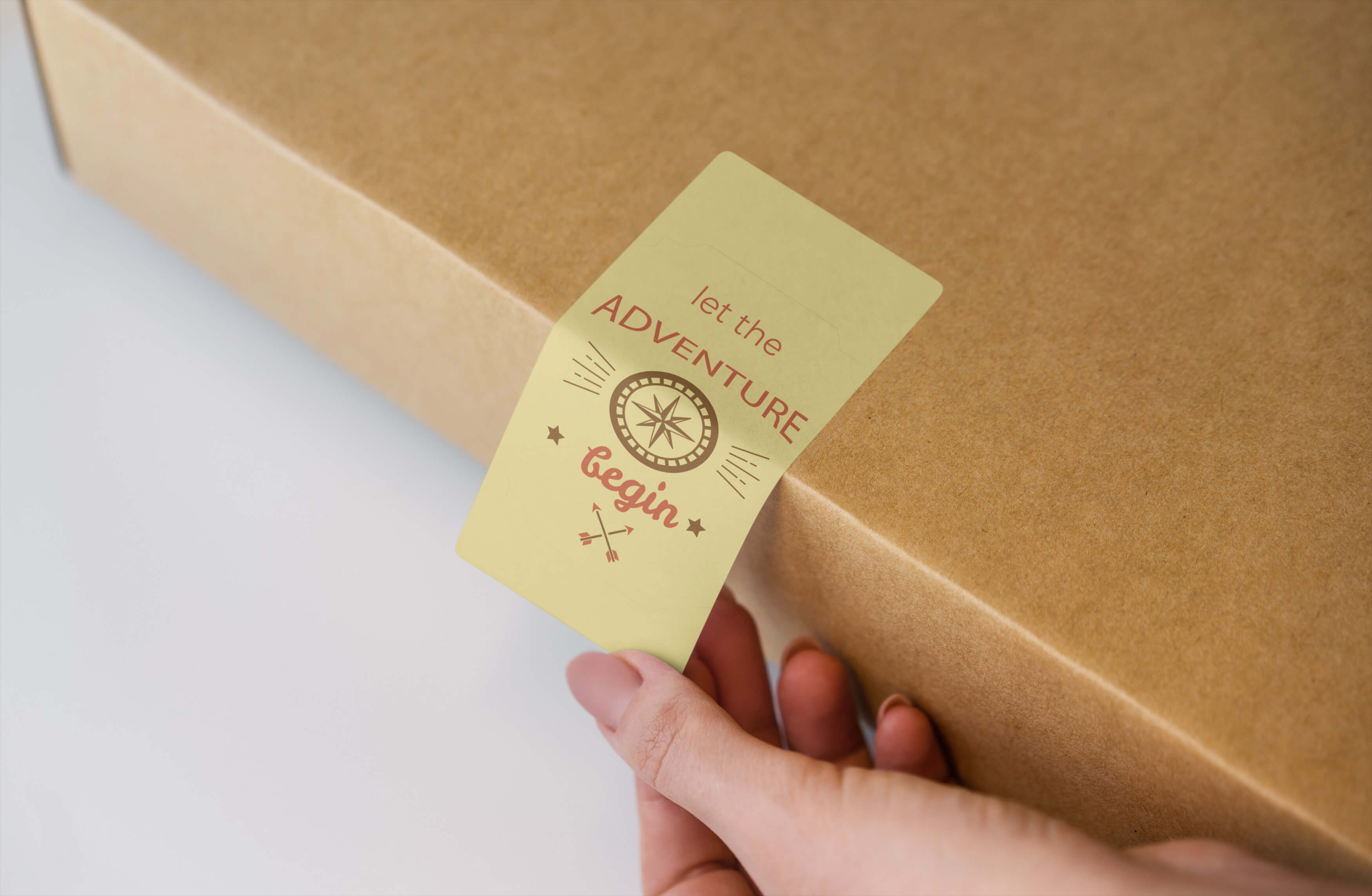 Hand holding a yellow tag with an adventure-themed design, attached to a brown box.