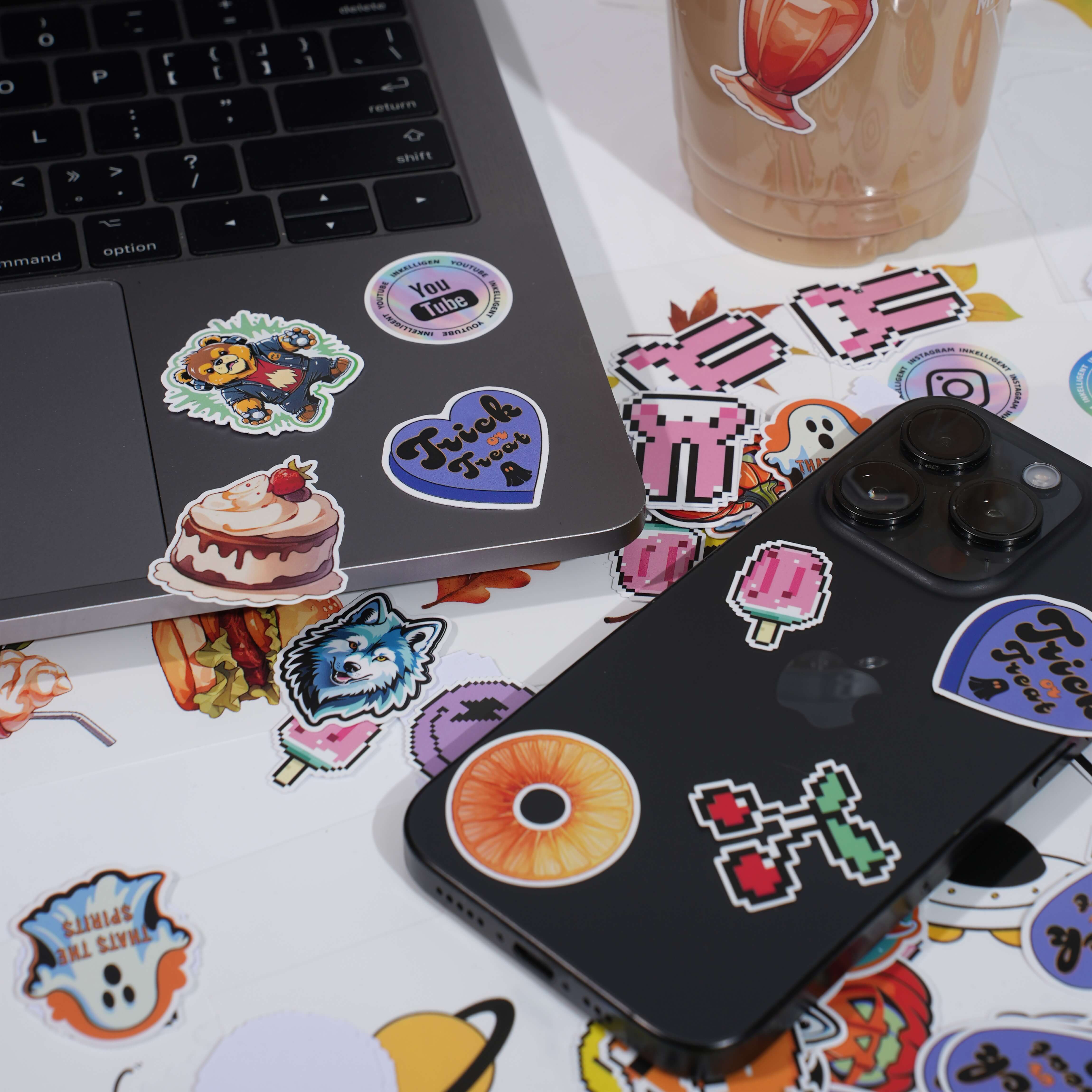 Laptop and phone decorated with colorful stickers, surrounded by more scattered stickers.