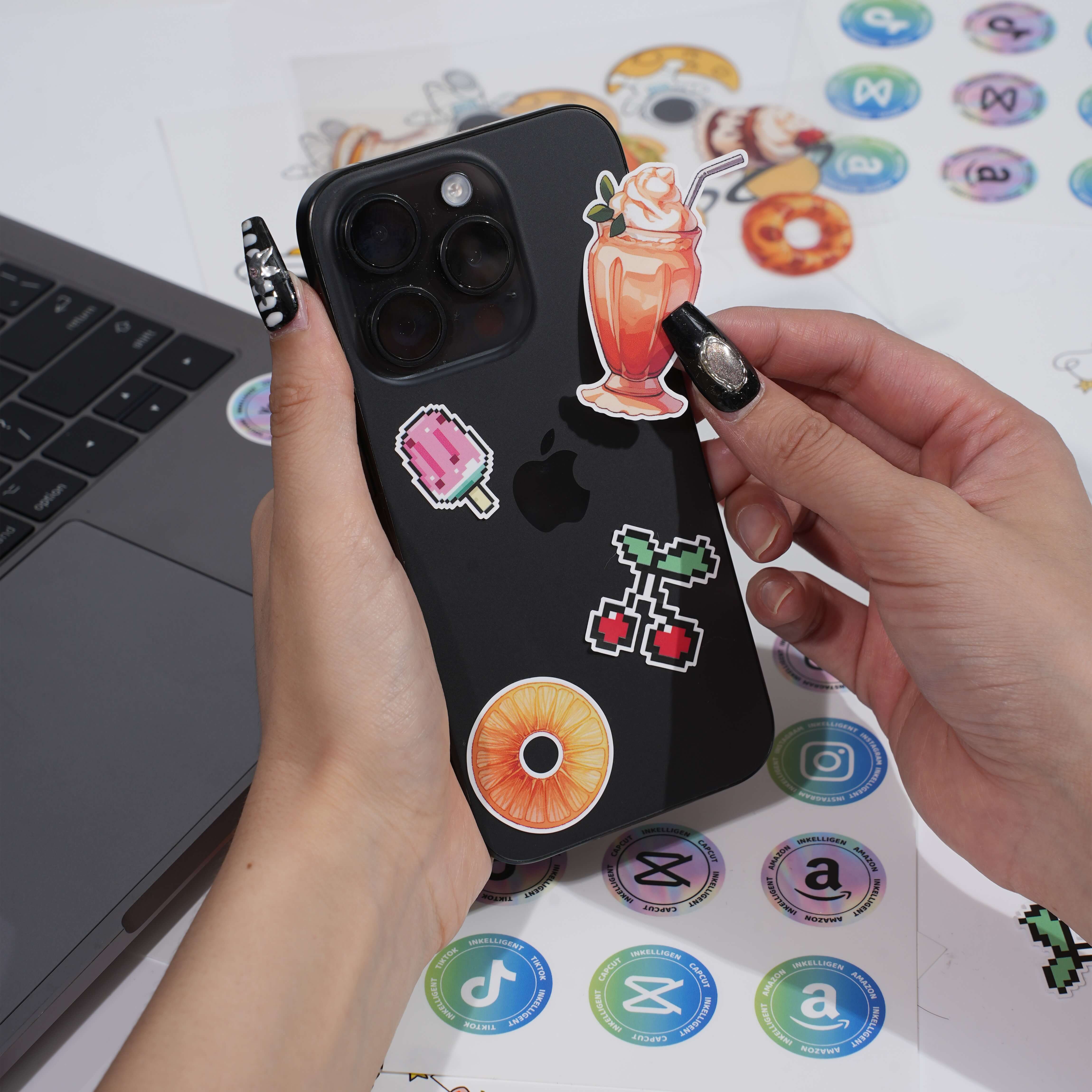 Decorating a black phone case with colorful stickers, laptop and more stickers in the background.